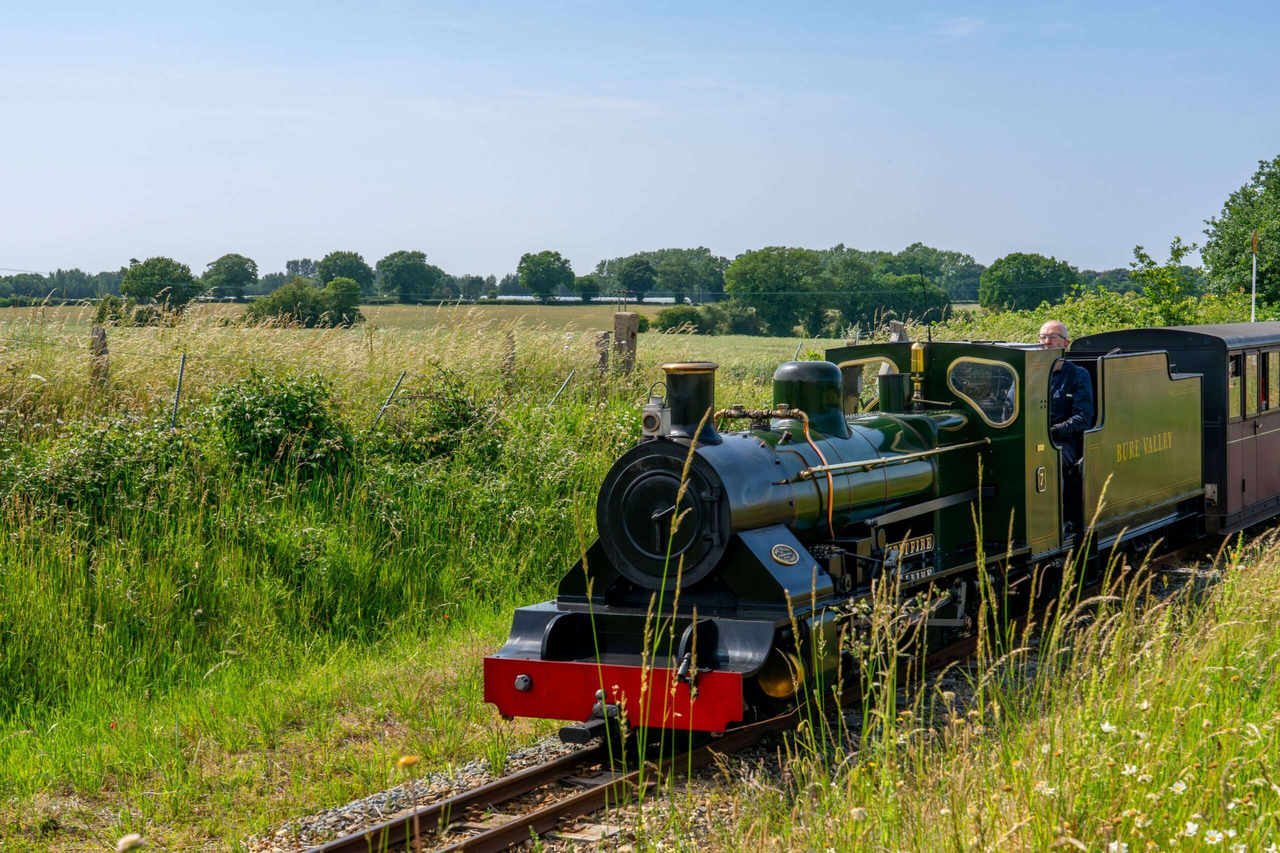 Bure Valley Railway steam train travelling through open Norfolk countryside on a sunny summer day.