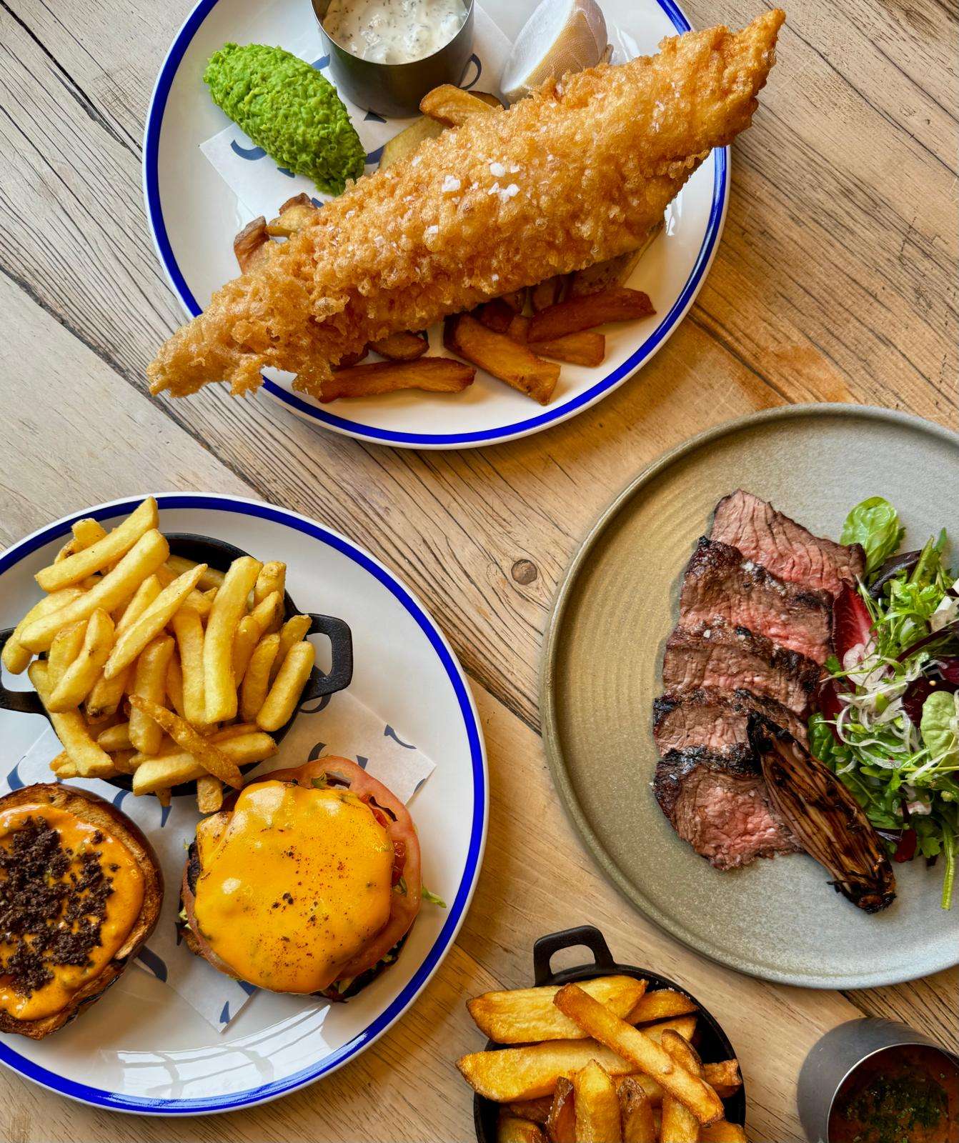 Traditional fish and chips burger and steak served with golden fries on a wooden table at the Swan Hotel Loddon