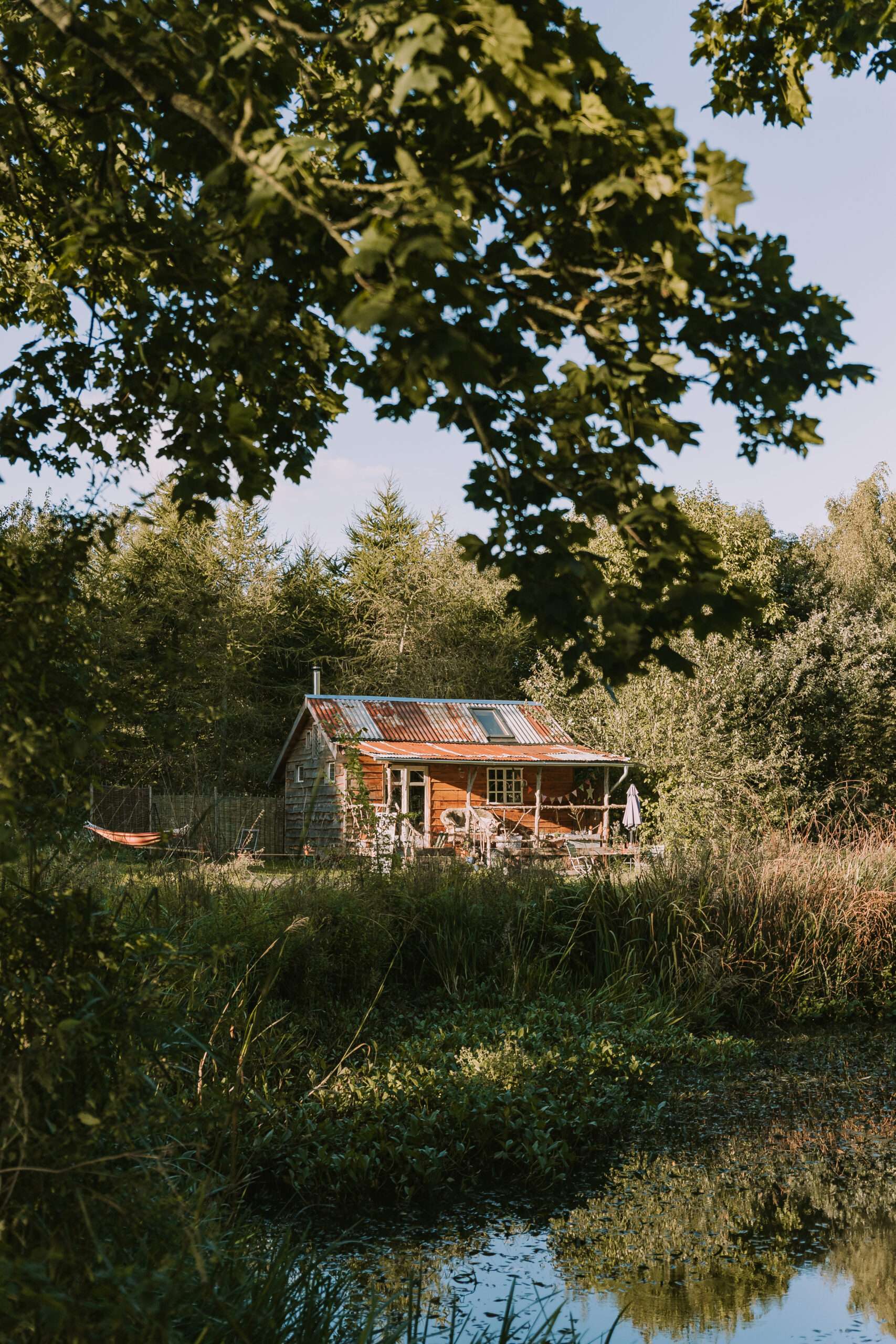 Rural waterside landscape with a wooden cabin reflected in a calm pond.