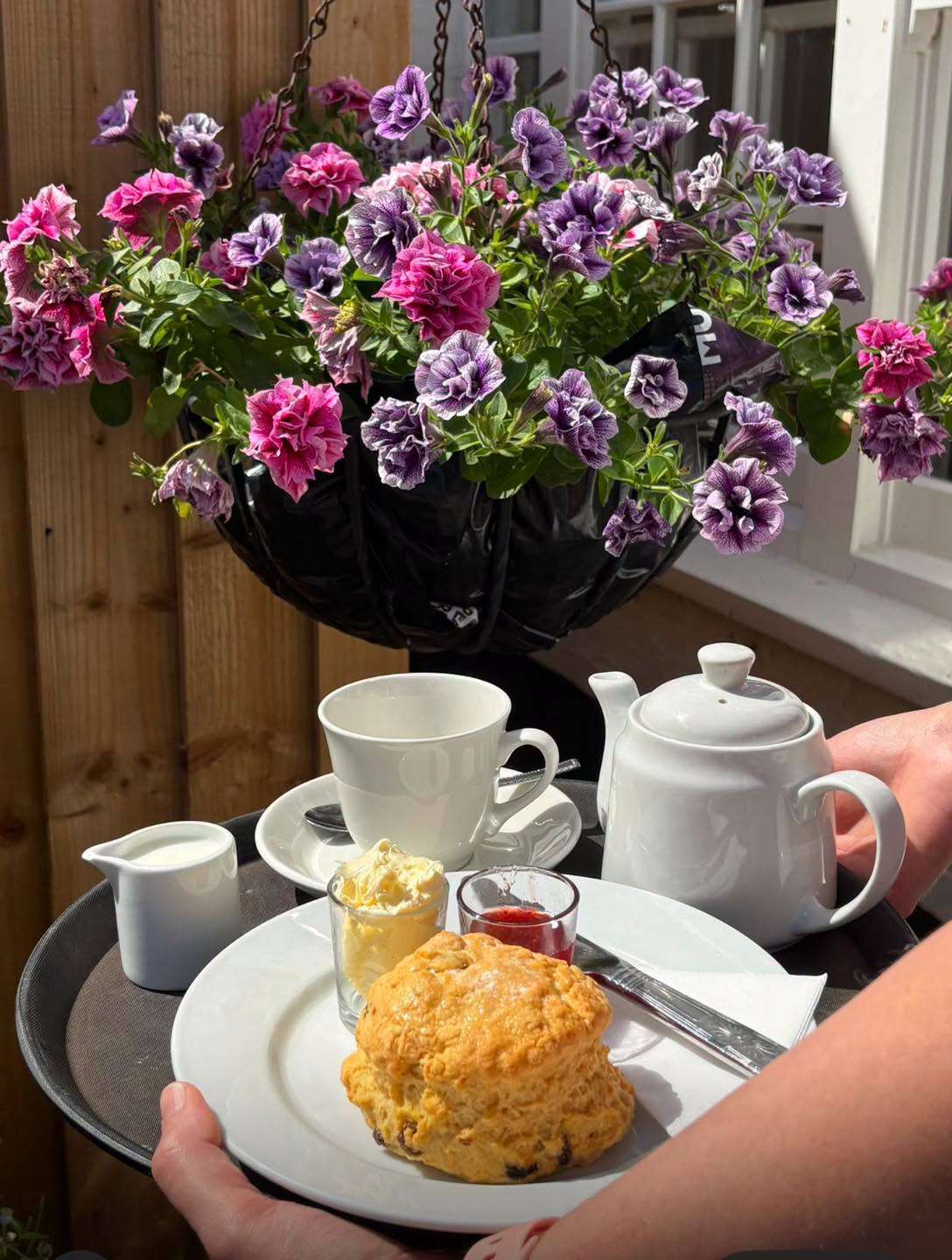 Cup of tea and teapot on a table beside a colourful hanging basket of flowers at Lincoln's Tea & Coffee House.