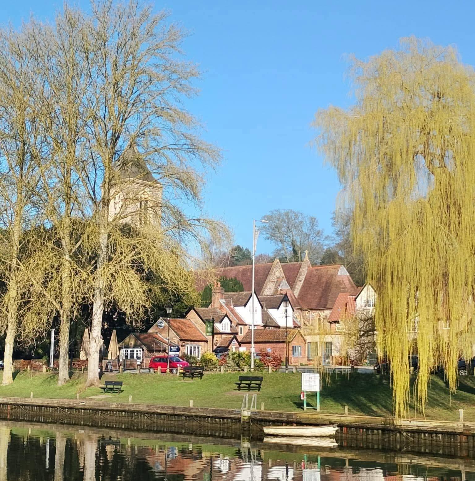 View across a riverside green towards Bridgestones restaurant in Thorpe St Andrew, surrounded by mature trees.