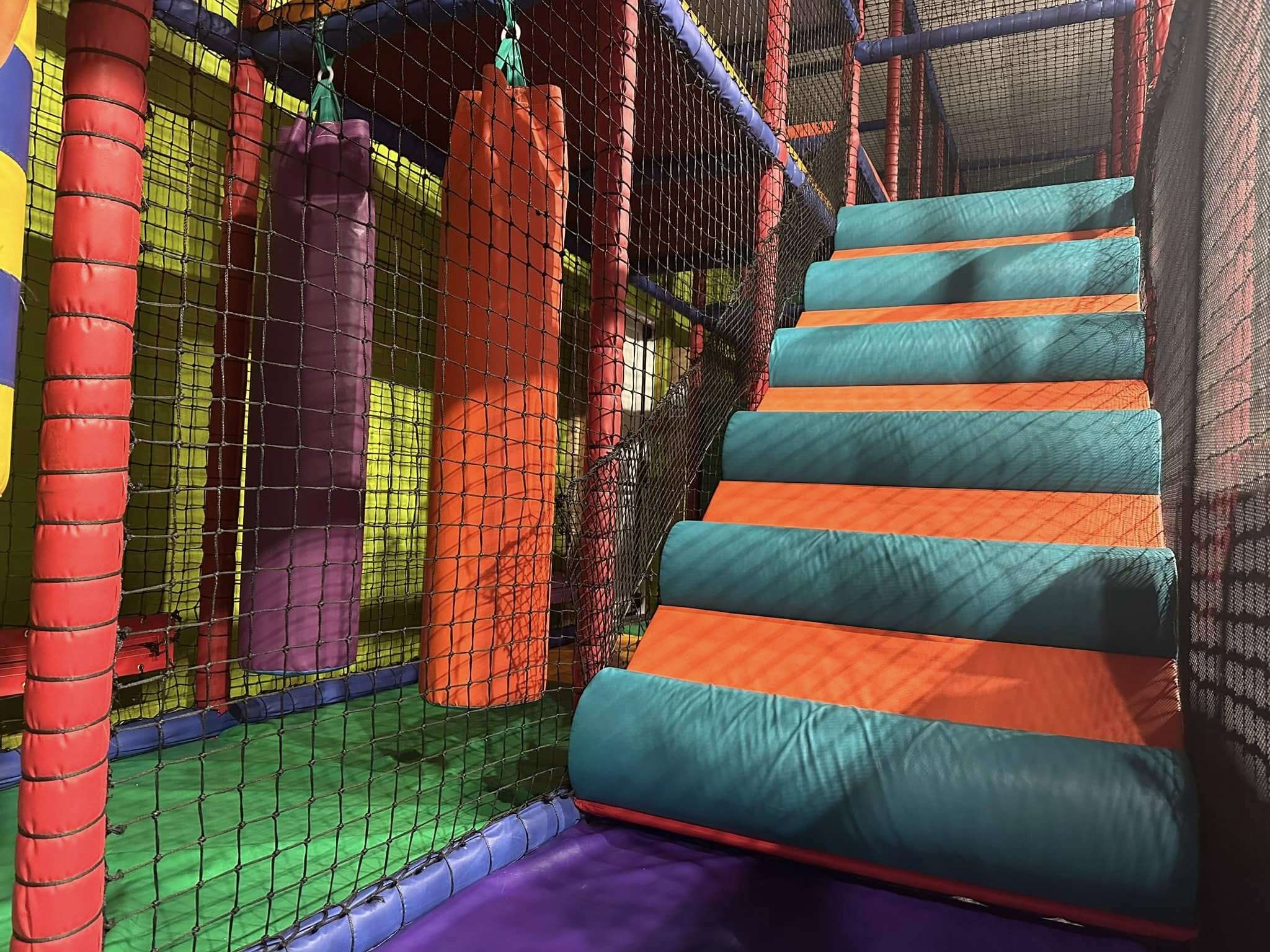 Multi-level soft play structure with padded obstacles, hanging rollers and brightly coloured climbing steps at The Jolly Junction.