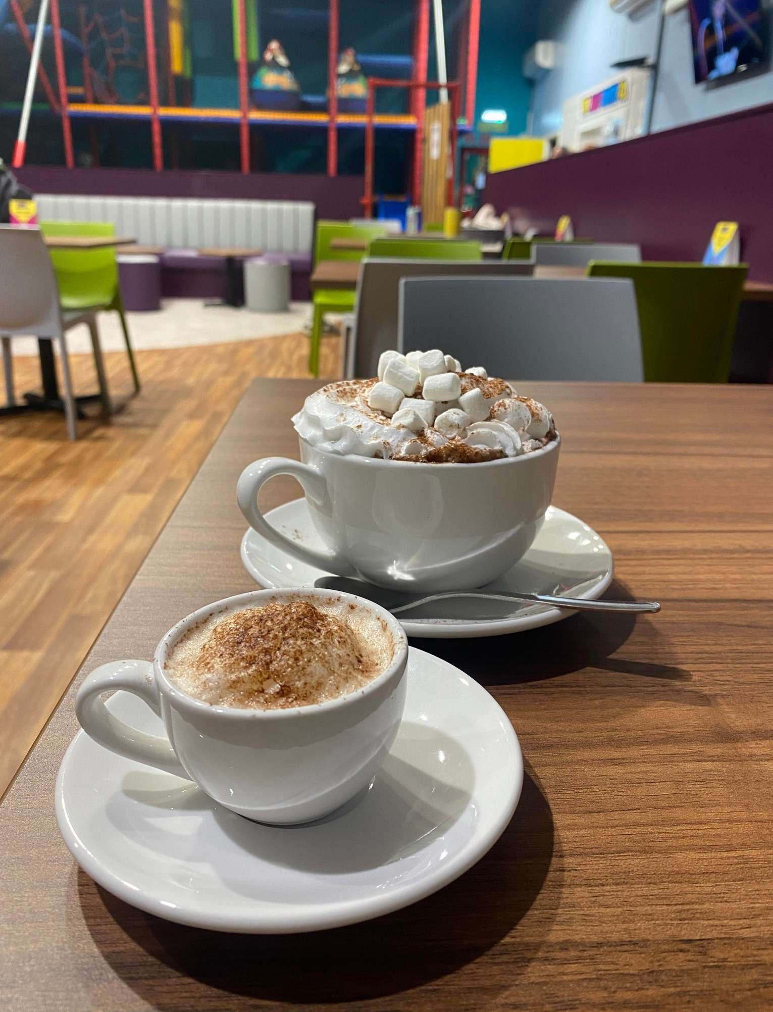 Cup of hot chocolate topped with whipped cream and chocolate sprinkles, served on a table at The Jolly Junction indoor play centre.